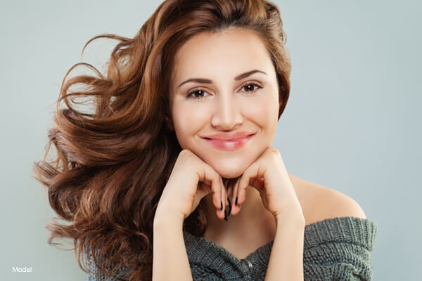 headshot of a smiling female model resting her head in her hands