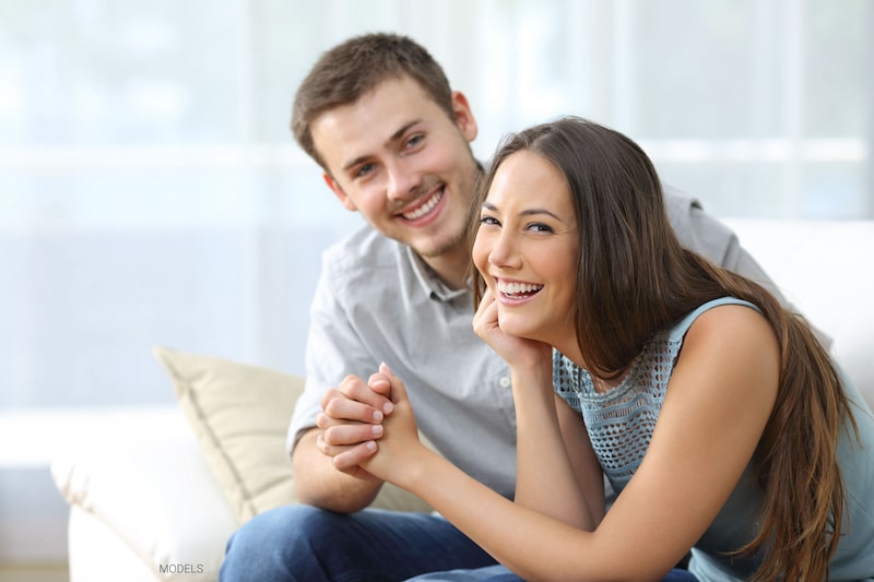 Attractive man and woman holding hands and smiling while sitting on a couch.