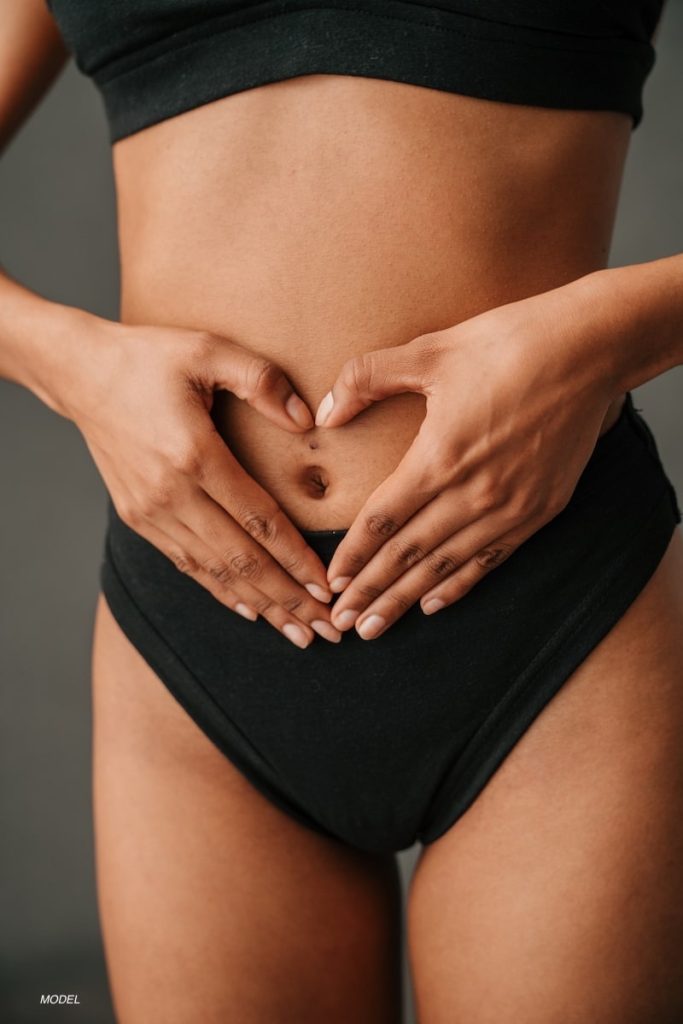 Close up of woman's toned midsection as she hold her hands in the shape of a heart over her stomach