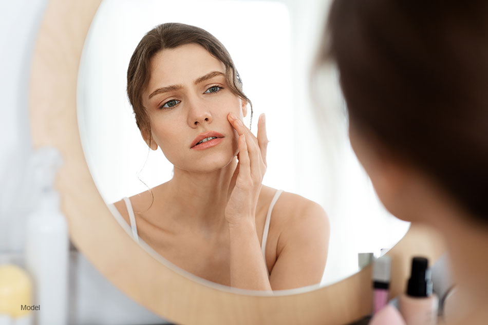 Acne prone skin concept. Upset young woman looking at mirror at home, checking her face skin